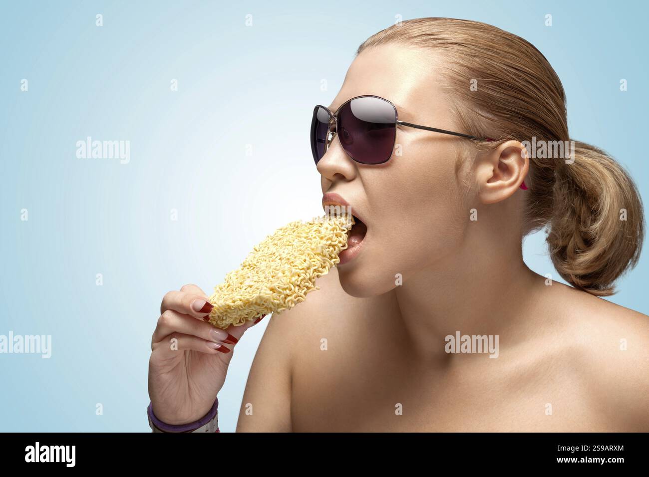 Un ritratto creativo di una bella donna affamata che mangia un blocco di spaghetti istantanei Foto Stock