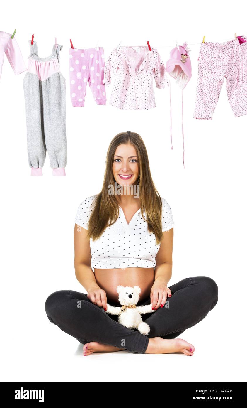 Giovani donne incinte e vestiti per bambini, su sfondo bianco Foto Stock
