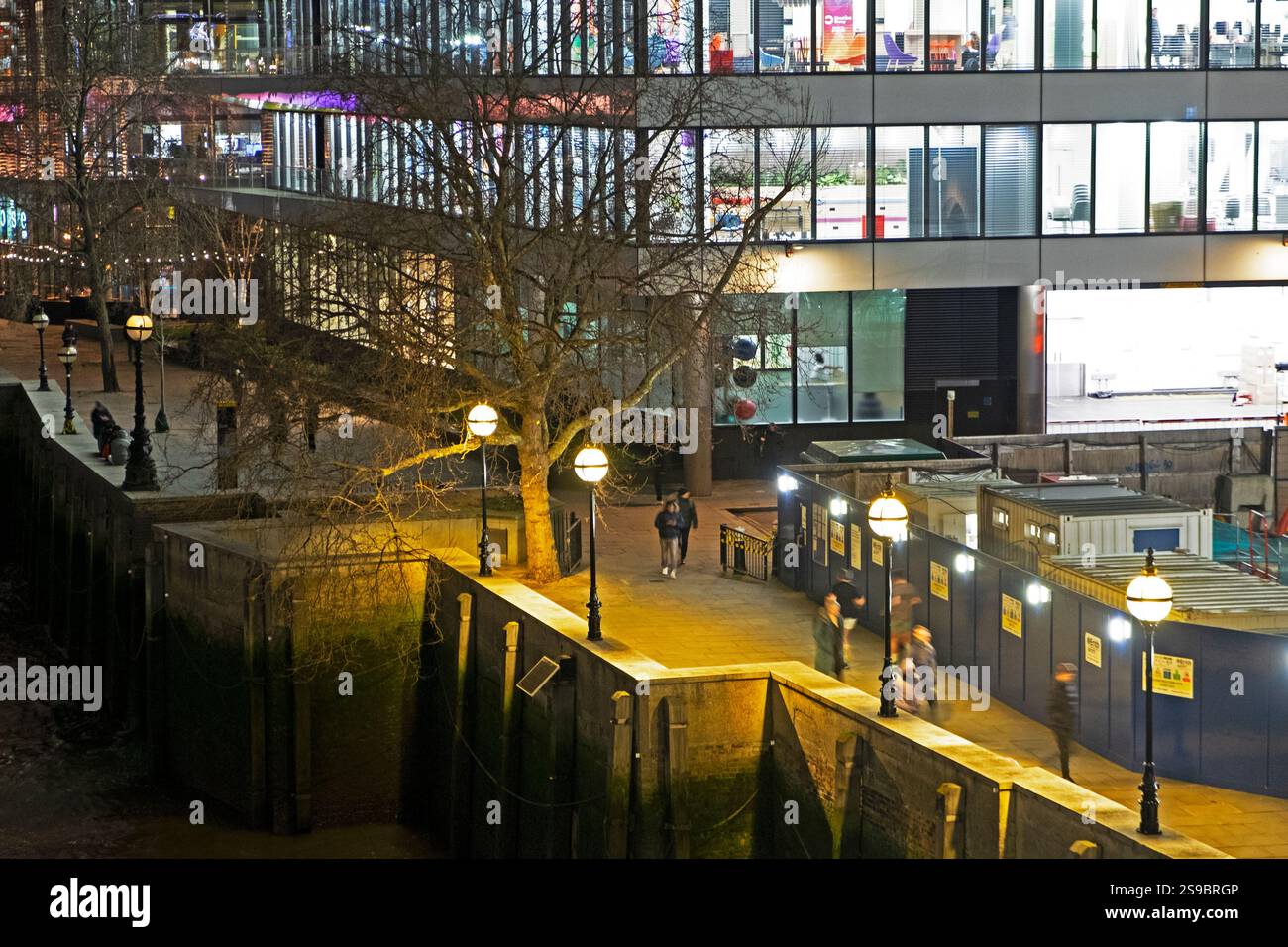 Le persone che camminano sul Tamigi di notte dopo il lavoro all'esterno illuminano edifici per uffici luci luminose per le strade in inverno Londra Regno Unito KATHY DEWITT Foto Stock