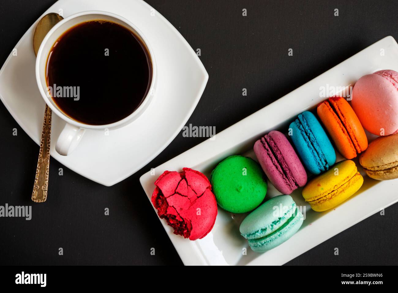 Una tazza di caffè bianco e macaron multicolore su un piatto bianco su sfondo nero. Tradizioni francesi Foto Stock Una tazza di caffè bianco e macaron multicolore su un piatto bianco su sfondo nero. Tradizioni francesi Foto Stock