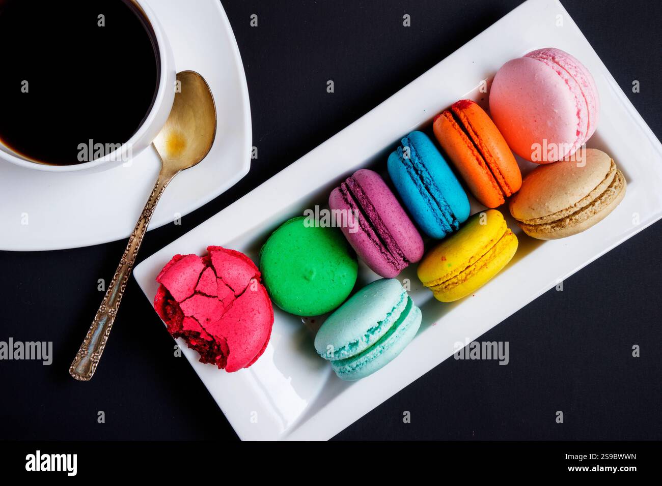 Una tazza di caffè bianco e macaron multicolore su un piatto bianco su sfondo nero. Tradizioni francesi Foto Stock Una tazza di caffè bianco e macaron multicolore su un piatto bianco su sfondo nero. Tradizioni francesi Foto Stock