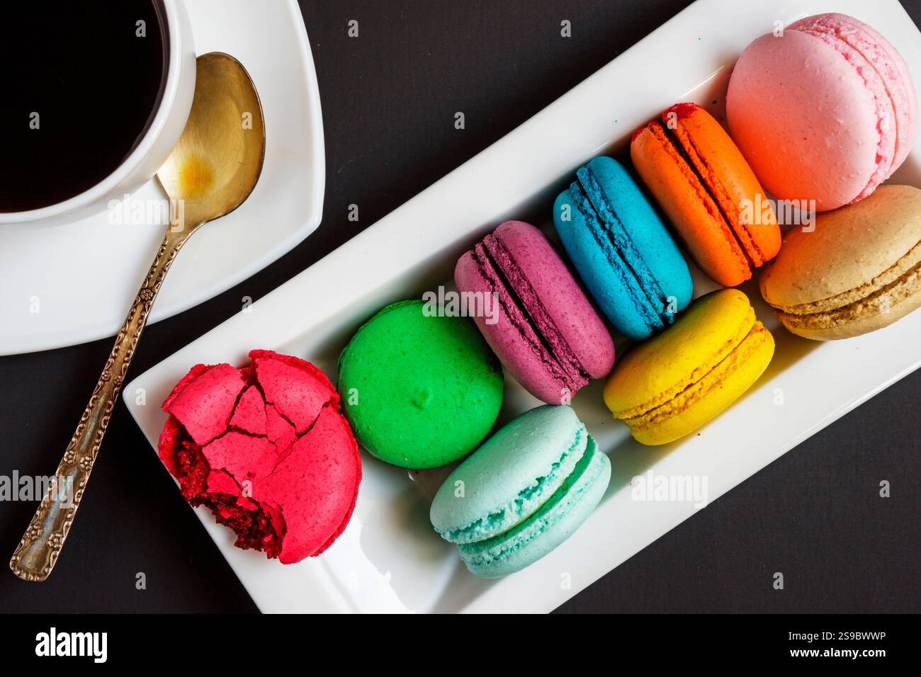 Una tazza di caffè bianco e macaron multicolore su un piatto bianco su sfondo nero. Tradizioni francesi Foto Stock Una tazza di caffè bianco e macaron multicolore su un piatto bianco su sfondo nero. Tradizioni francesi Foto Stock