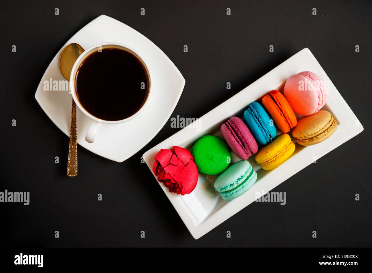 Una tazza di caffè bianco e macaron multicolore su un piatto bianco su sfondo nero. Tradizioni francesi Foto Stock Una tazza di caffè bianco e macaron multicolore su un piatto bianco su sfondo nero. Tradizioni francesi Foto Stock