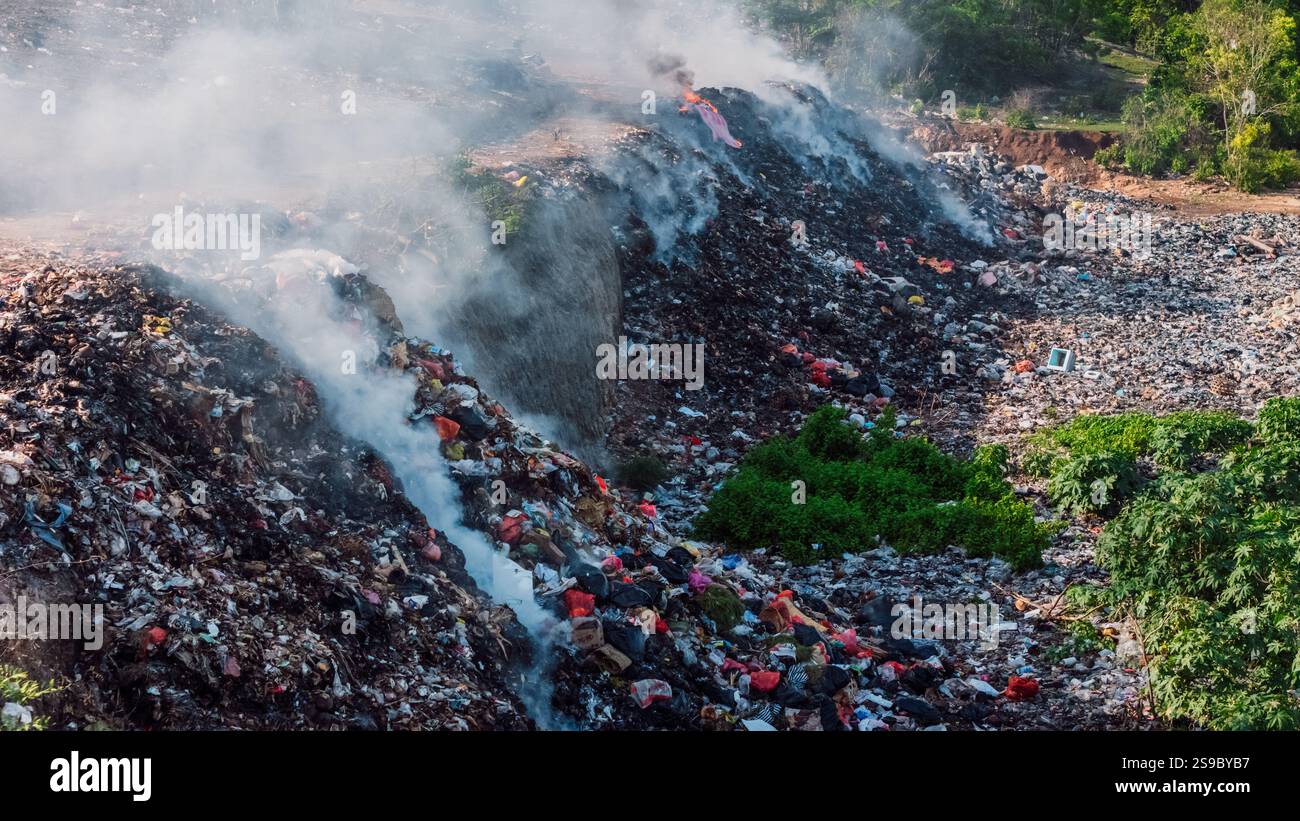 Bruciare le discariche che emettono fumo, evidenziando le sfide legate all'inquinamento ambientale e alla gestione dei rifiuti in un paesaggio naturale Foto Stock