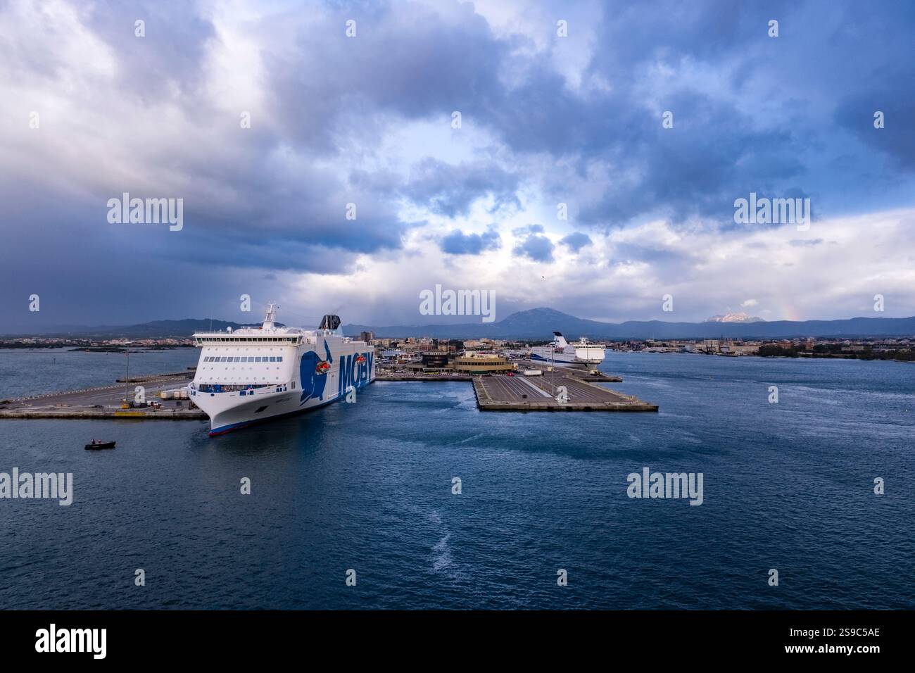 Il traghetto Moby Legacy of Moby Lines all'ancora nel porto di Olbia, ospita la città in lontananza. Foto Stock