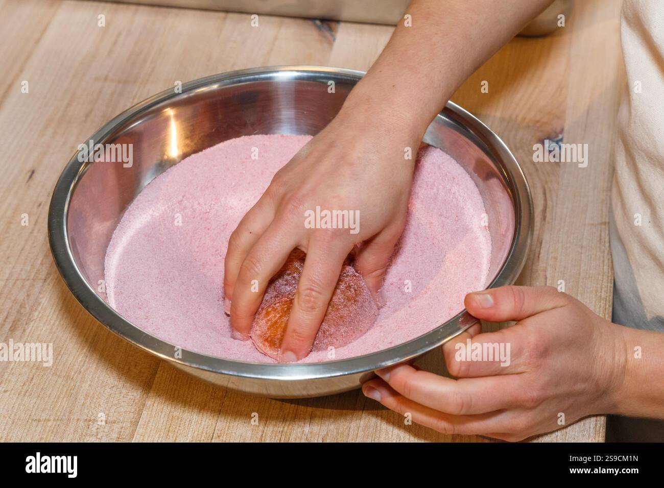 Ciambella ricoperta a mano in zucchero rosa in una ciotola di miscelazione in acciaio Foto Stock