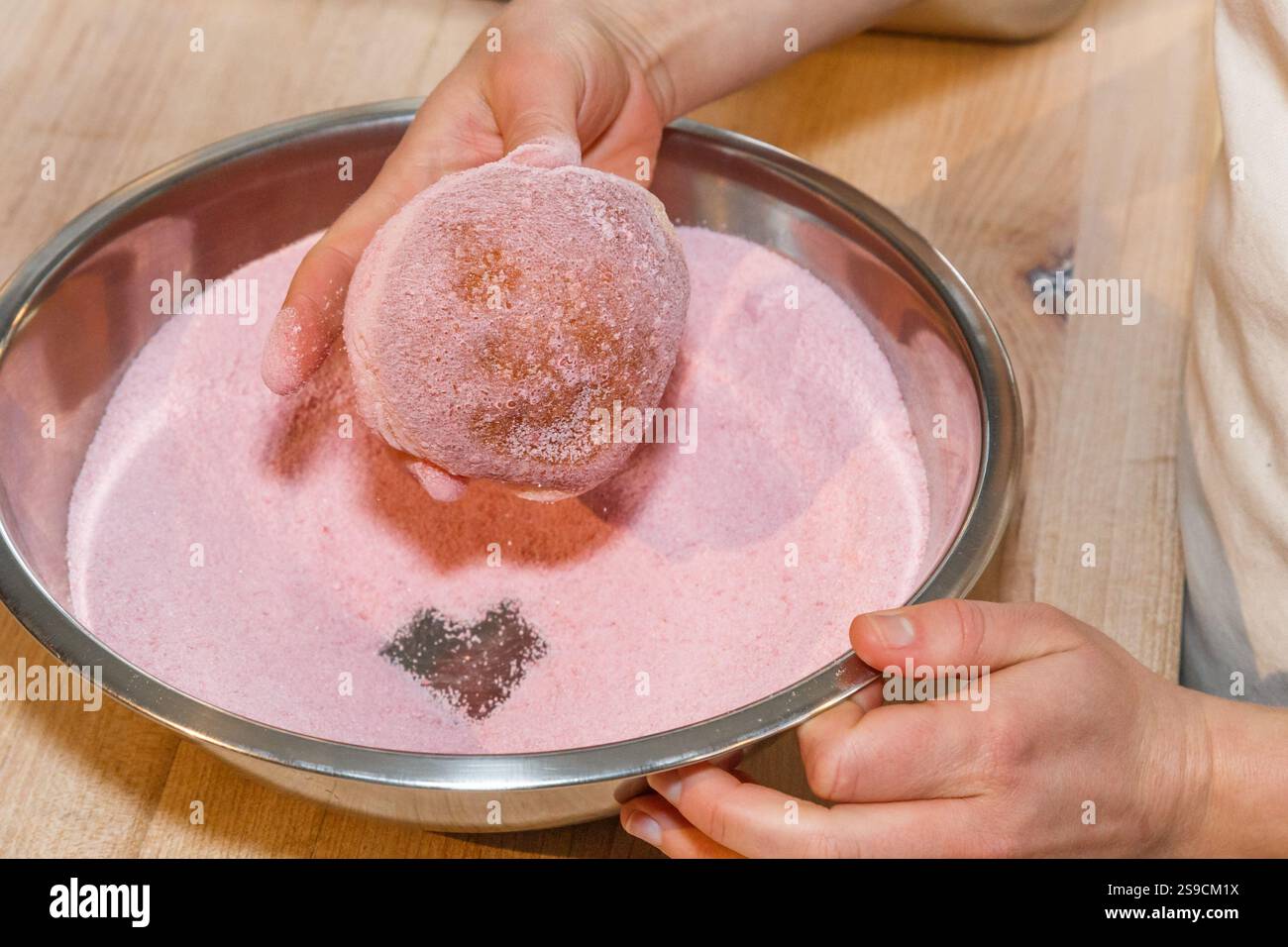 Ciambella ricoperta a mano in zucchero rosa in una ciotola di miscelazione in acciaio Foto Stock