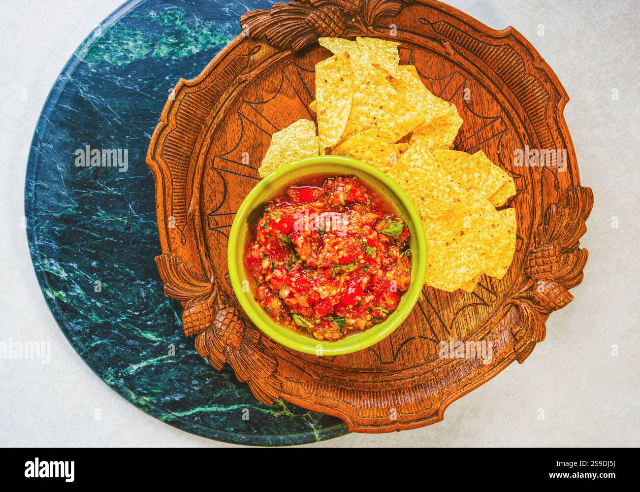 Potrai ammirare la salsa fresca fatta in casa con pomodori biologici e basilico in una ciotola vintage e le patatine di mais biologico su un antico vassoio di legno Foto Stock