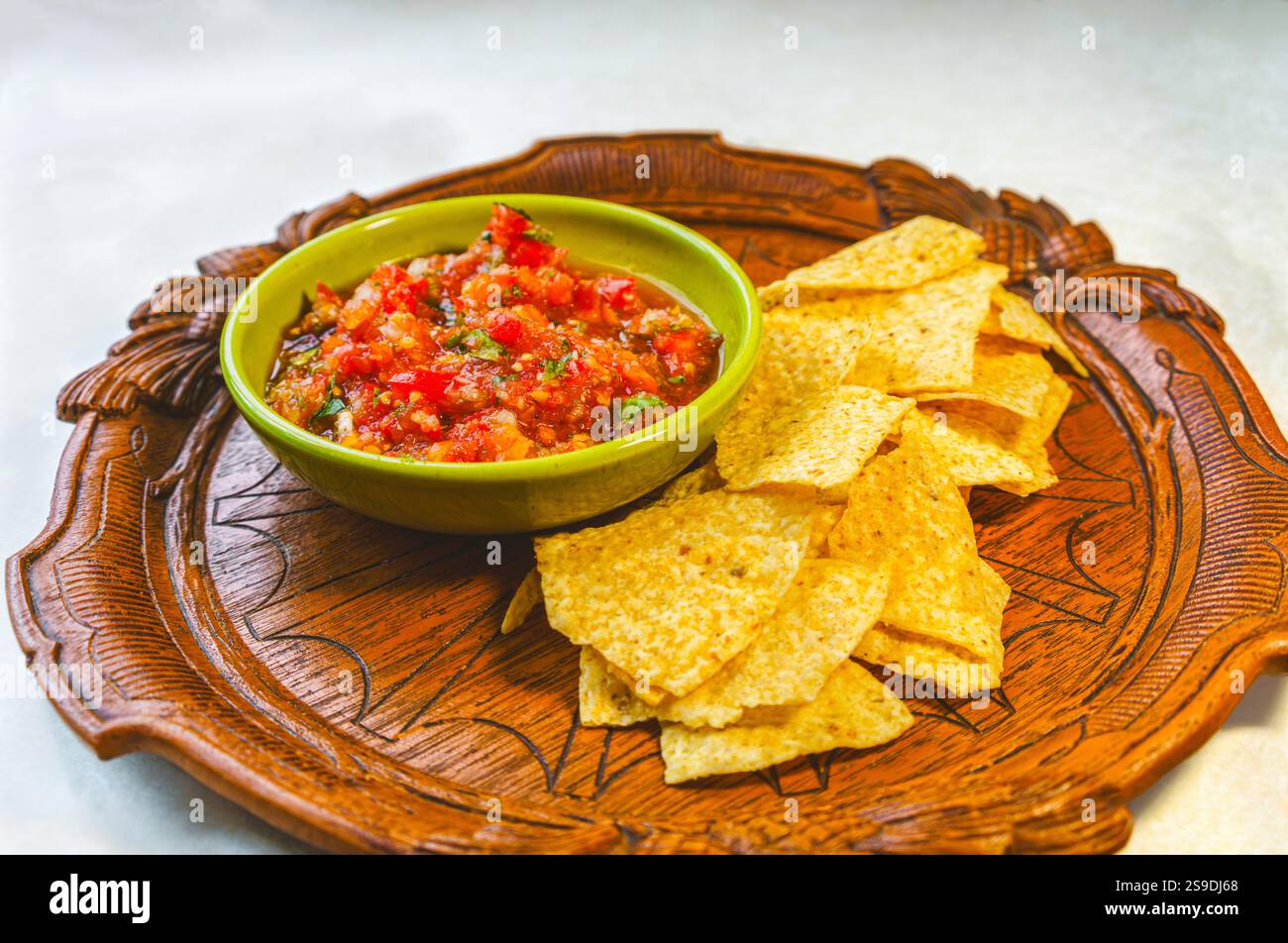 Salsa fresca fatta in casa da pomodori e basilico biologici in una ciotola vintage e patatine di mais biologico su un antico vassoio di legno Foto Stock