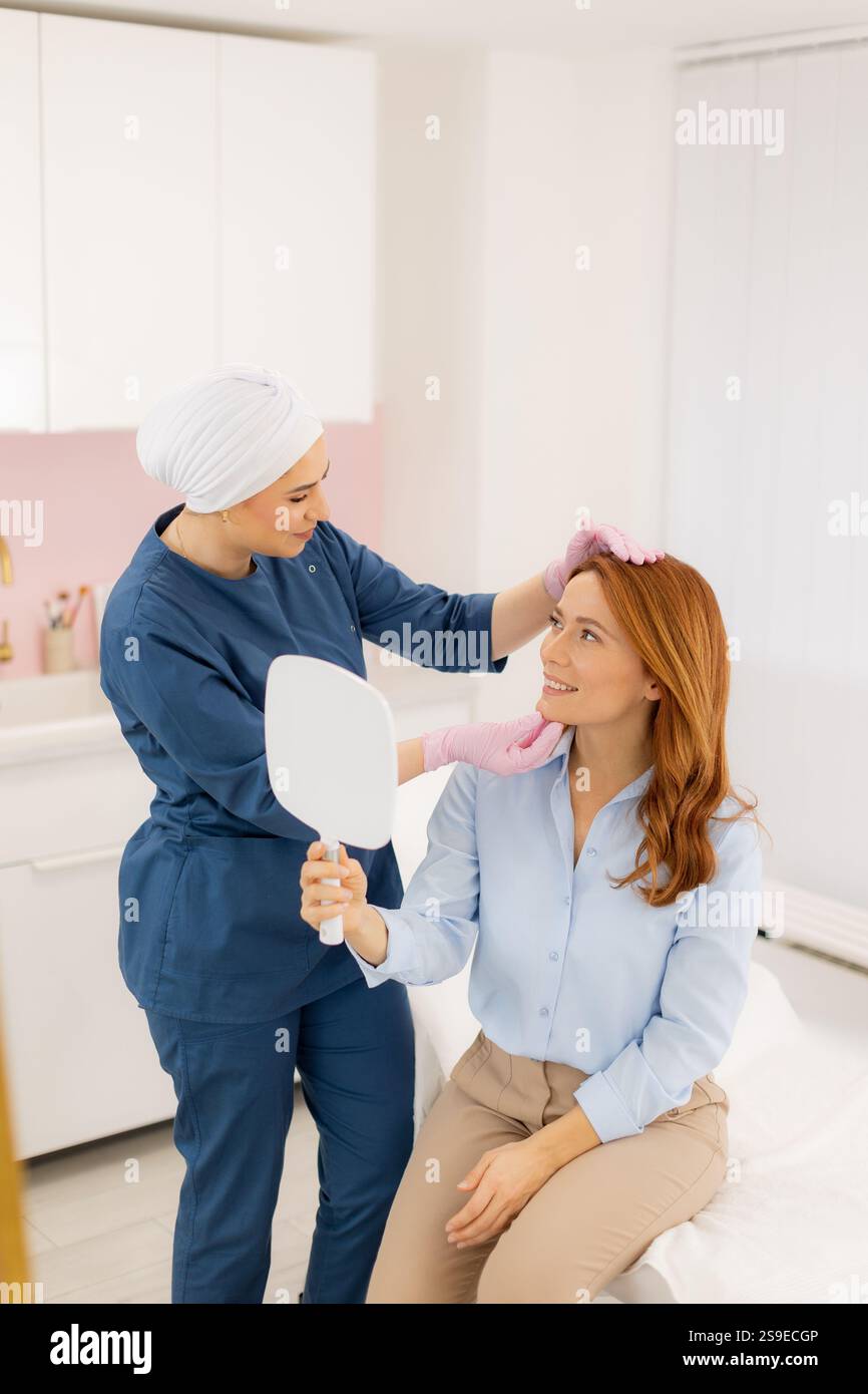 Un estetista esperto fornisce una consulenza personalizzata per la cura della pelle, acconciando delicatamente i capelli del cliente mentre ammira il suo riflesso radioso. Naturale l Foto Stock