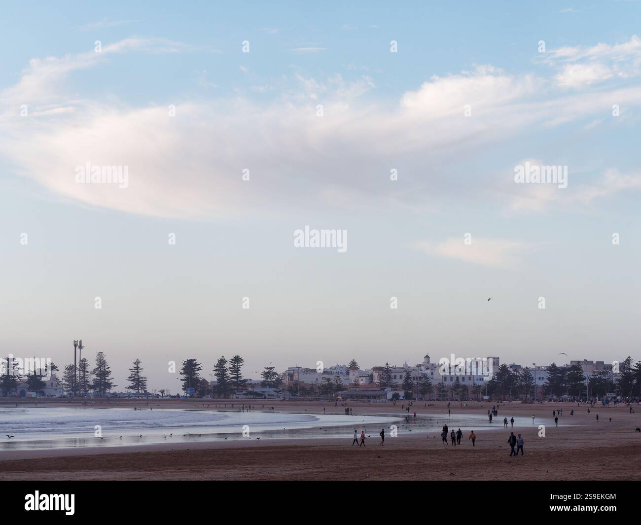 Persone sulla spiaggia di sabbia una sera con la Medina storica bianca e le nuvole alle spalle nella città di Essaouira, in Marocco. 25 gennaio 2025 Foto Stock