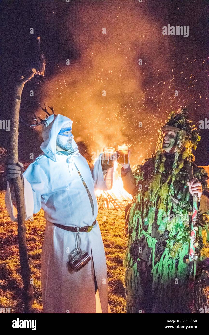 Due uomini vestiti da Green Man e un pagano reggono bicchieri di sidro davanti a un falò in una festa del villaggio di Wassail in Inghilterra Foto Stock