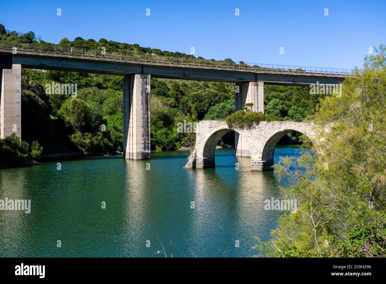 Un ponte stradale in cemento attraversa un affluente del lago San Sebastiano, con il vecchio ponte in pietra in primo piano. Foto Stock