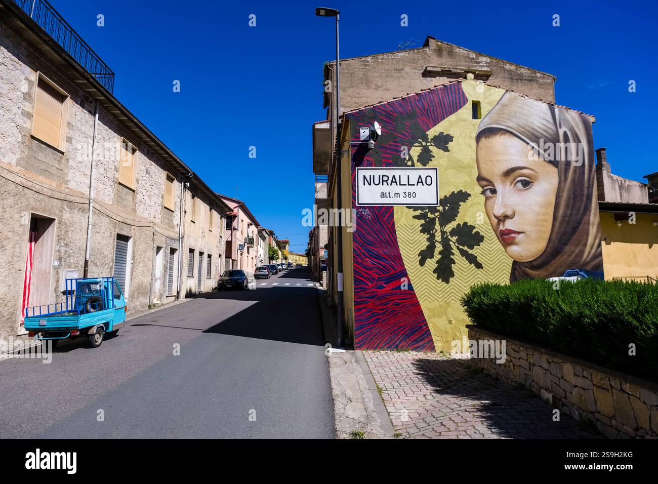 Cartello d'ingresso al paese di Nurallo come parte di un grande graffito con il ritratto di una giovane donna. Foto Stock