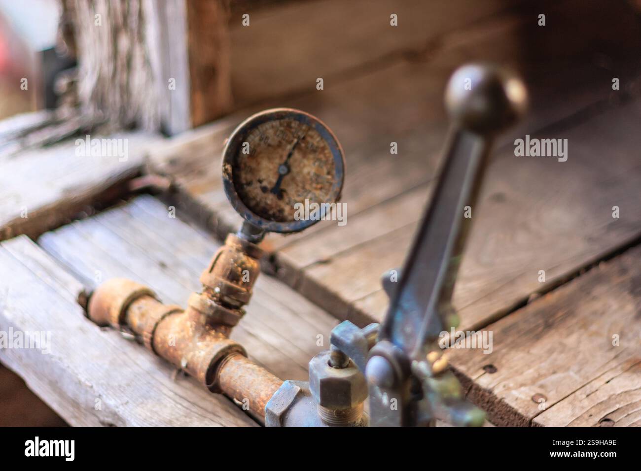 Un vecchio manometro arrugginito si trova su una superficie di legno. L'indicatore è vecchio e usurato, con una superficie nera e uno stelo in metallo arrugginito. Anche la superficie in legno lo è Foto Stock