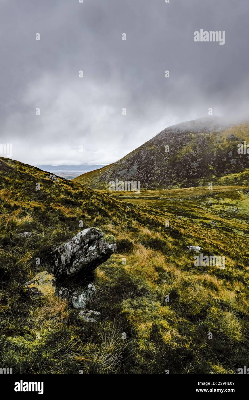 Cielo coperto sopra un terreno collinare marrone e verde. Diverse rocce sono prominenti in primo piano. La scena sembra un po' arida. Foto Stock