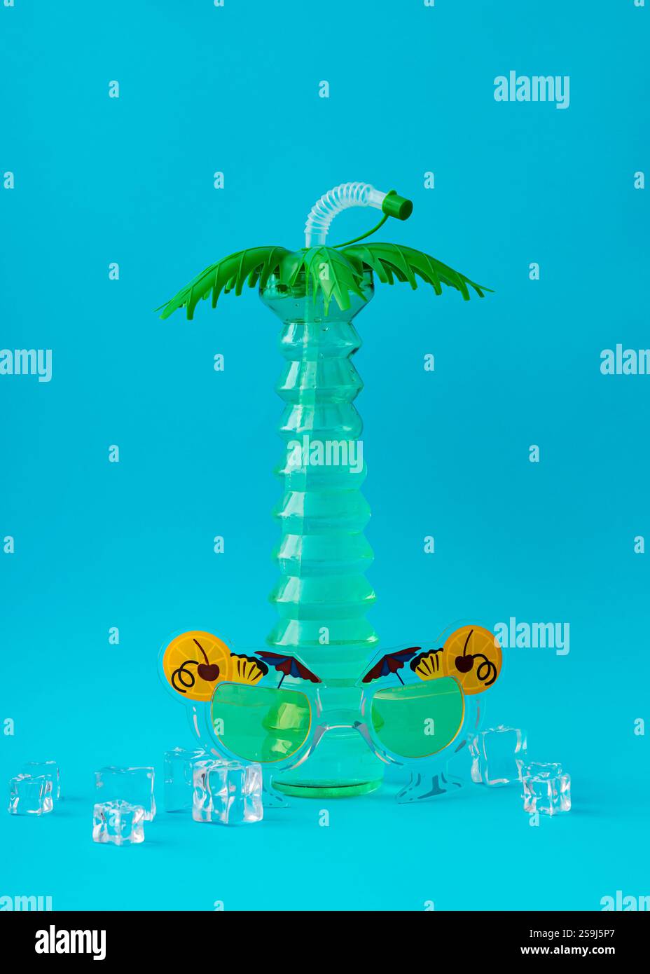 Layout creativo estivo con bicchiere da cocktail con palme, occhiali da sole per feste e cubetti di ghiaccio su sfondo azzurro. Un cocktail party sulla spiaggia minimalista. Foto Stock