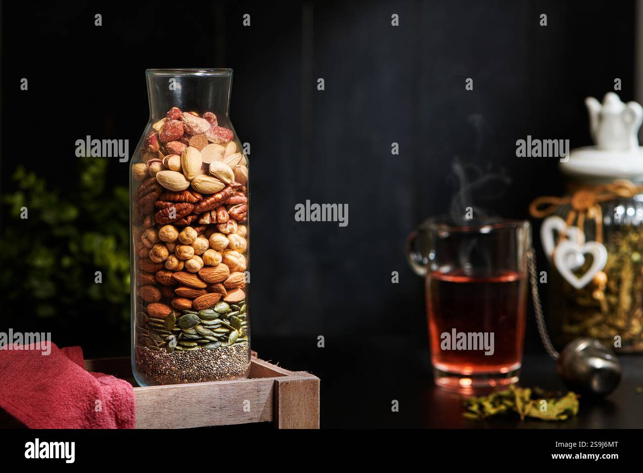 Mix di noci in un bellissimo vaso di vetro con un bicchiere di tè sullo sfondo. Semi, noci, arachidi, pecan, mandorle, anacardi, pistacchio, albicocca, Rai Foto Stock