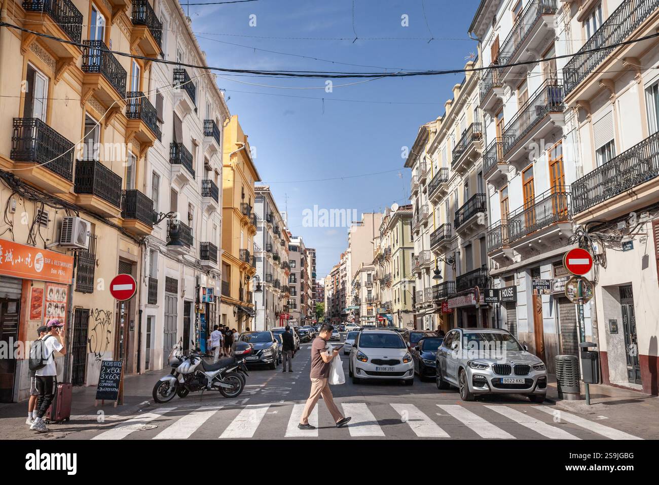 VALENCIA, SPAGNA - 13 OTTOBRE 2024: Un uomo attraversa un passaggio pedonale nel centro della città in una giornata di sole, circondato da facciate storiche, auto parcheggiate Foto Stock