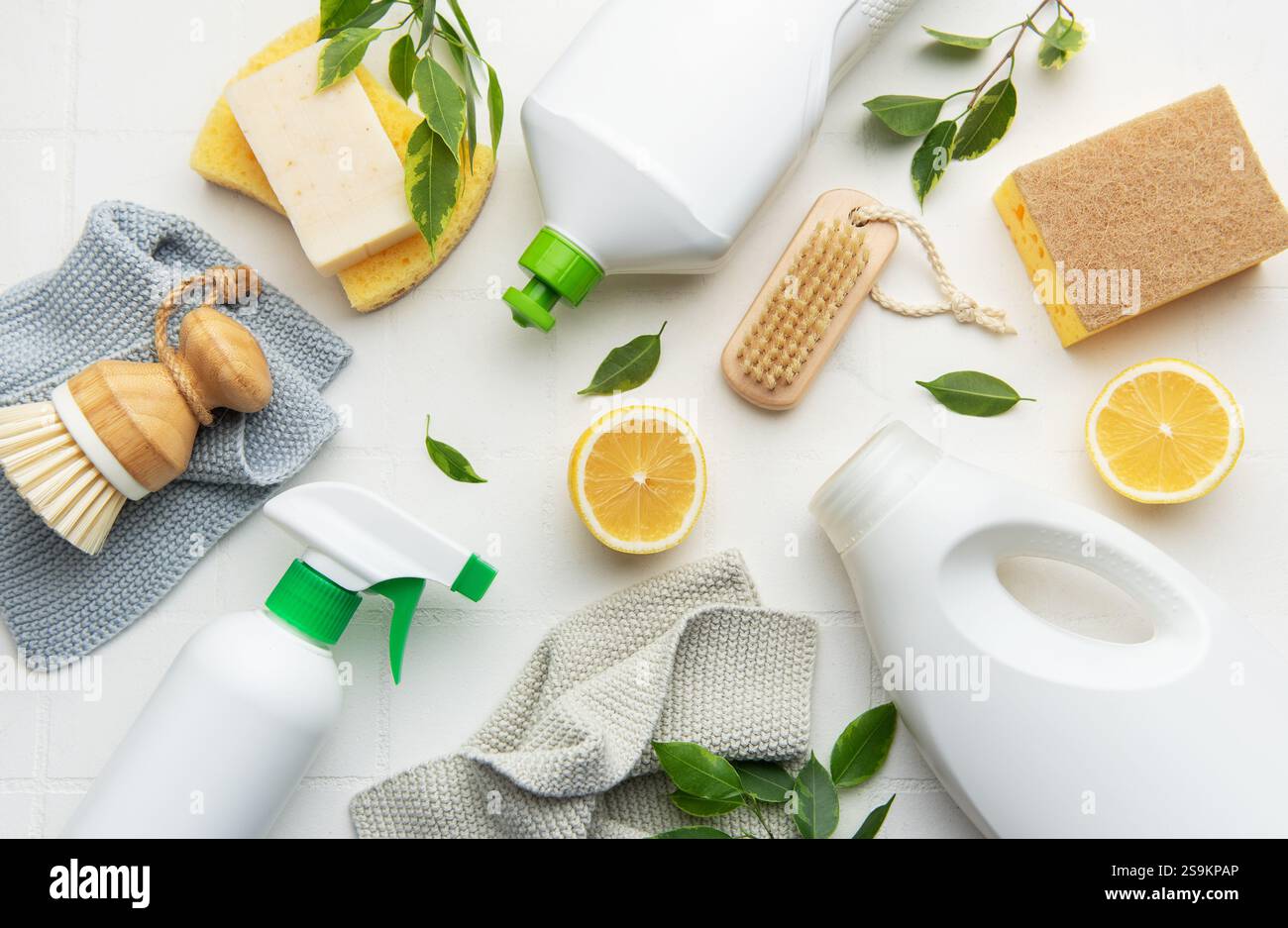 Prodotti per la pulizia naturali, fette di limone, spazzole e spugne disposte su una superficie bianca per una pulizia eco-consapevole Foto Stock