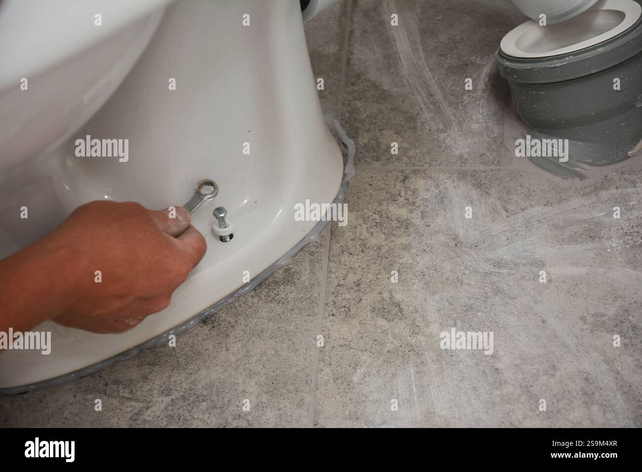 L'idraulico installa il WC sul sigillante al silicone e lo fissa in posizione Foto Stock