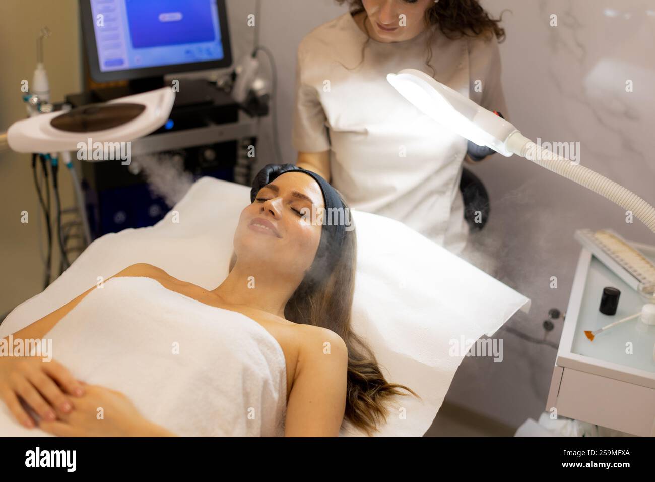 Un tranquillo ambiente spa presenta una donna che si gode un trattamento viso, con nebbia che avvolge il suo viso. L'atmosfera favorisce il relax e la cura della pelle Foto Stock