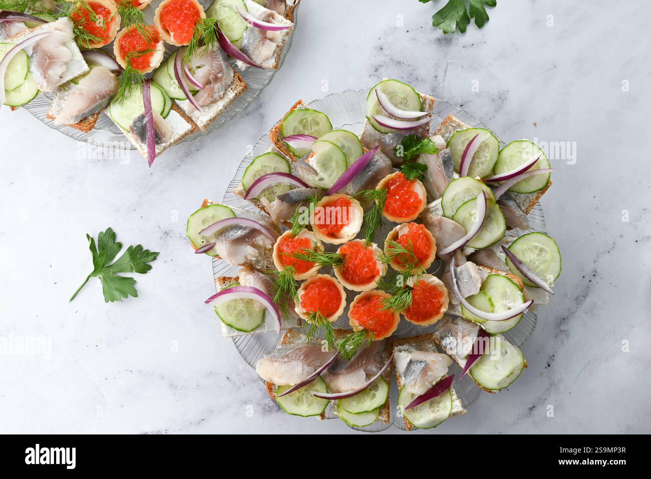 Panini a vista con vari condimenti come cetriolo, cipolla, pesce e caviale su un piatto bianco. Realizzato con diversi tipi di pane, guarnito con d Foto Stock