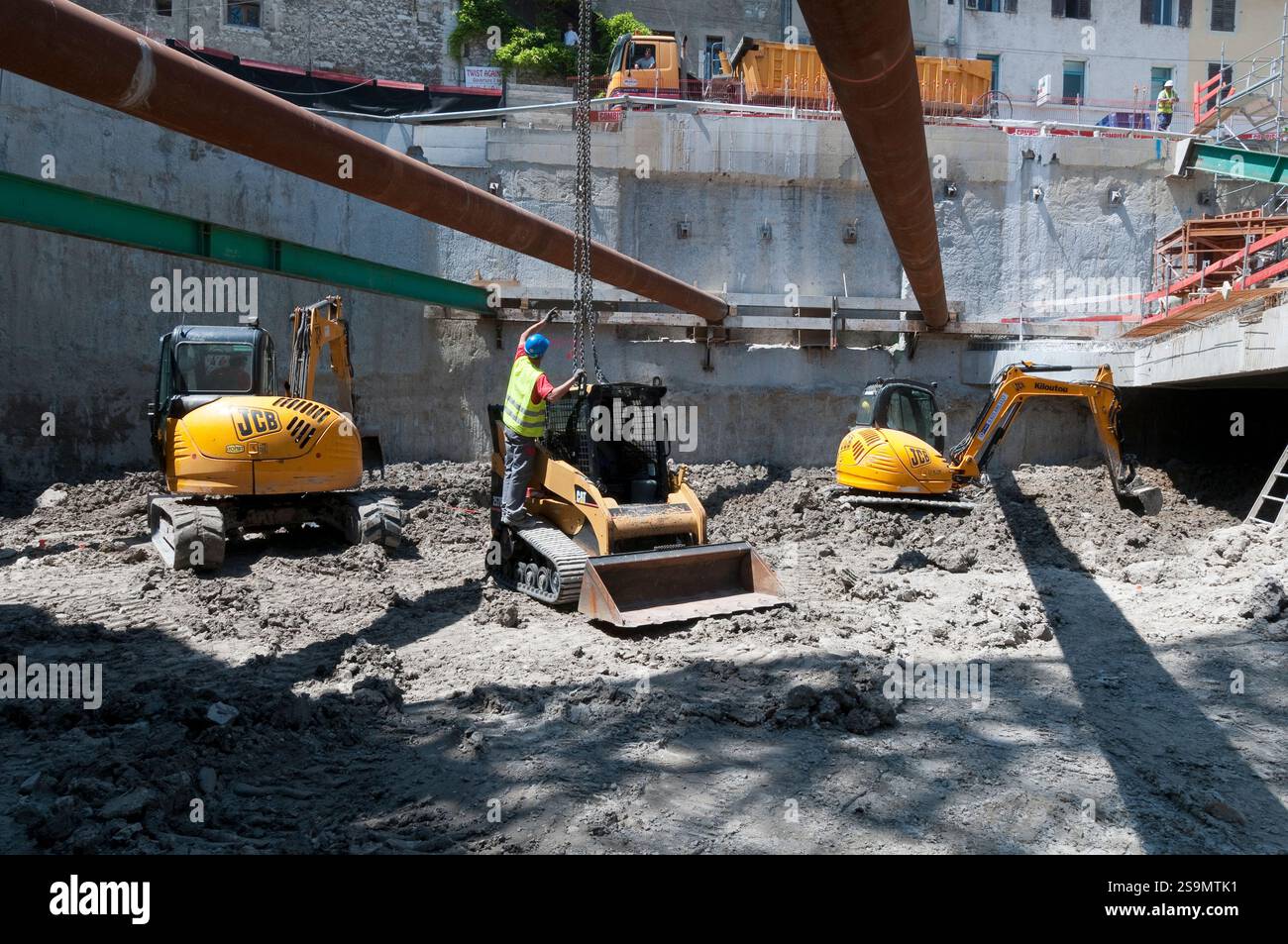 Scavo di un parcheggio sotterraneo in città, con mini attrezzature di movimento terra. Con le mura. Foto Stock