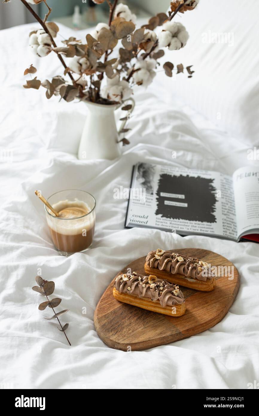 Eclari, caffè, libro aperto, fiori secchi. Colazione a letto Foto Stock