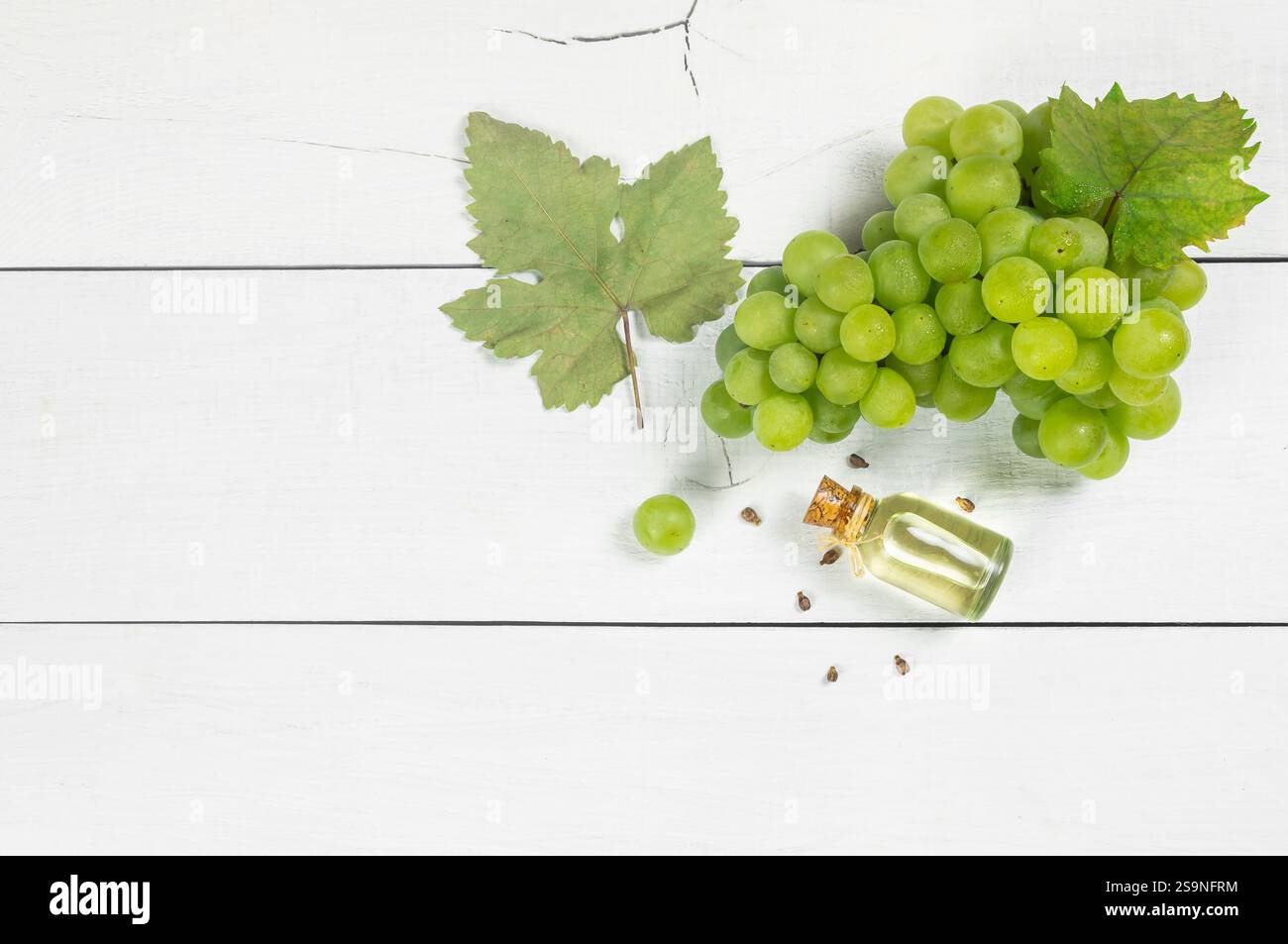 Bottiglia in vetro di olio di semi d'uva con uva verde fresca frutta su sfondo bianco di legno Foto Stock