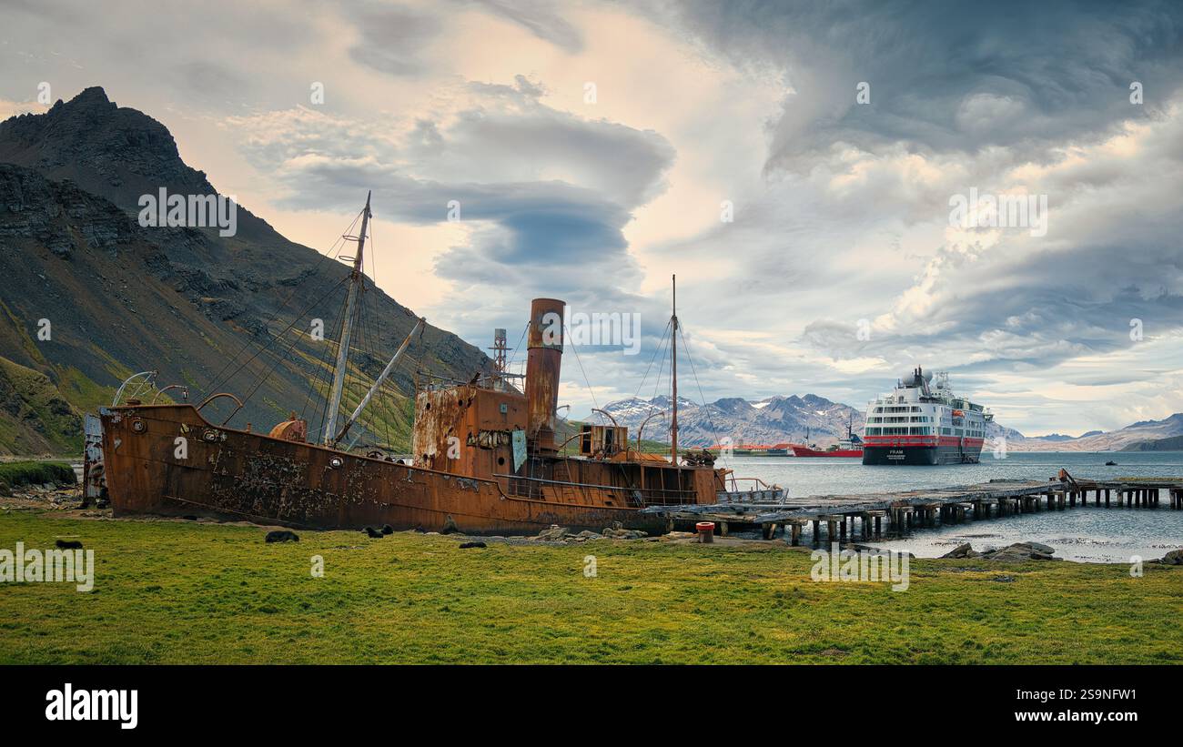 Un'antica barca arrugginita che contrasta con una moderna nave da crociera nel porto di Grytviken, Georgia del Sud. Foto Stock
