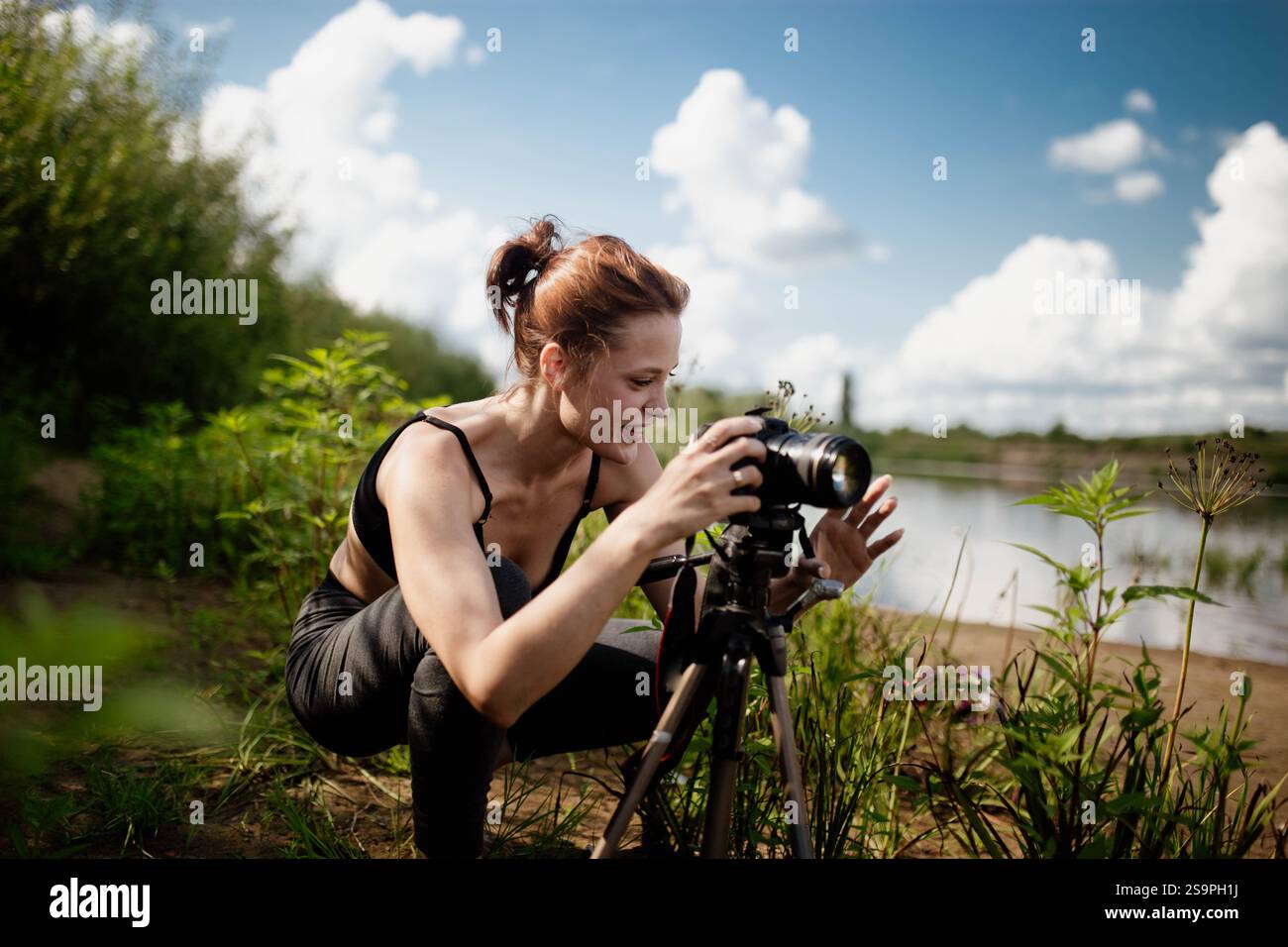 Una donna sorride mentre regola la macchina fotografica sul lungolago sotto un cielo blu Foto Stock