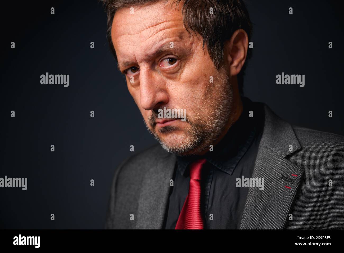 Ritratto di un imprenditore adulto maturo con rughe sulla fronte in elegante tuta grigia con camicia nera e cravatta rossa con messa a fuoco selettiva Foto Stock