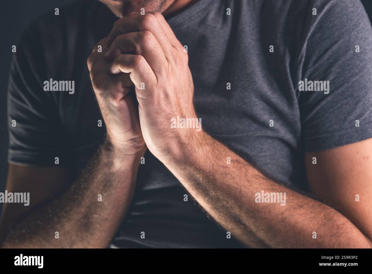 L'uomo cristiano che prega a Dio in camera oscura con mani aggrappate, primo piano con fuoco selettivo Foto Stock