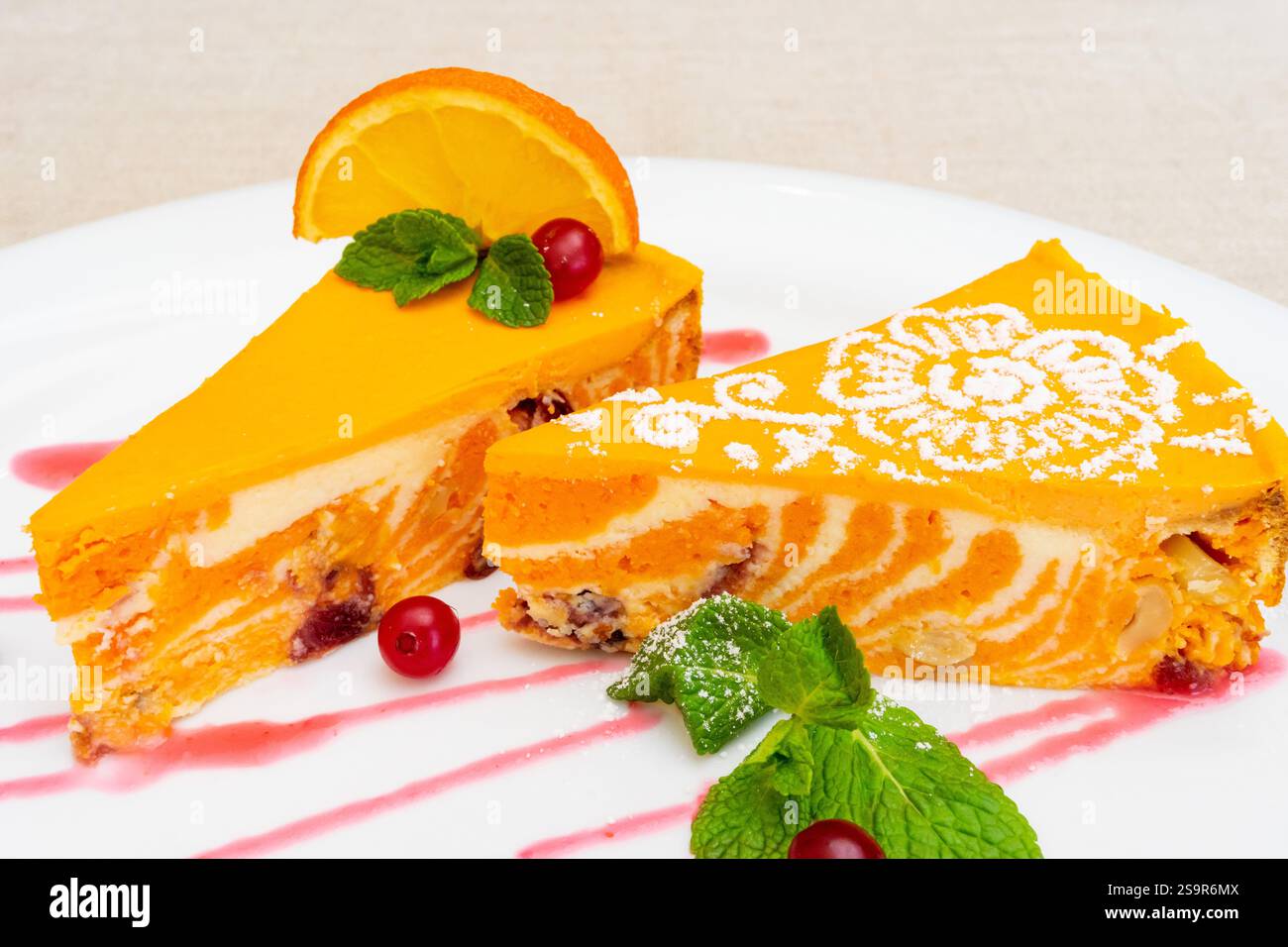 Due fette di dessert arancione splendidamente placcate mostrano colori vivaci. Sono guarnite con foglie di menta, frutti di bosco e un filo decorativo, creat Foto Stock