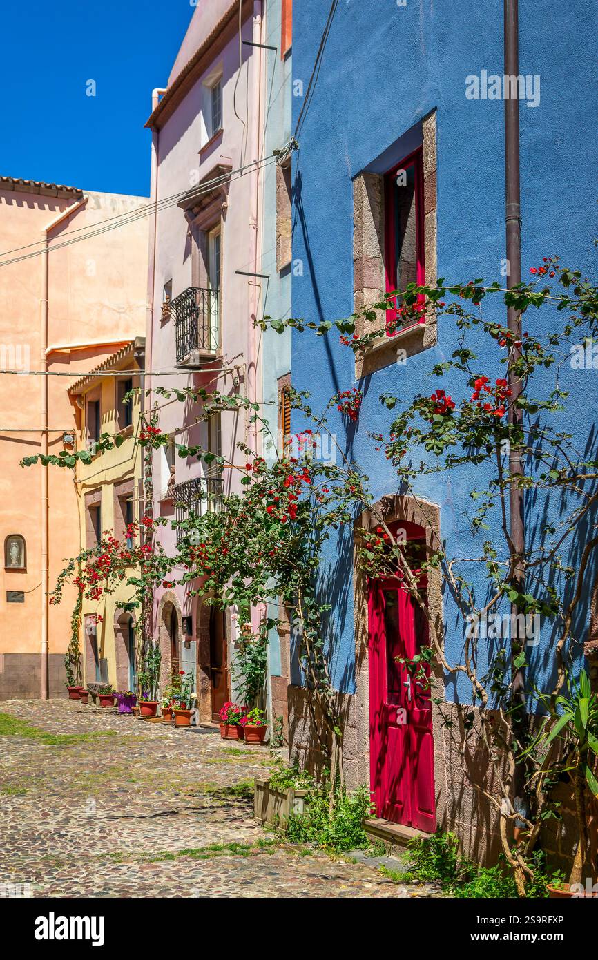 Case colorate con vasi di fiori e bouganville in una pittoresca strada acciottolata nell'antico villaggio mediterraneo di Bosa, isola della Sardegna, Italia Foto Stock