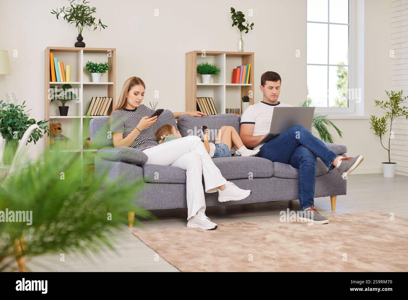 Famiglia che utilizza computer portatili e telefoni durante il tempo libero sul divano di casa Foto Stock