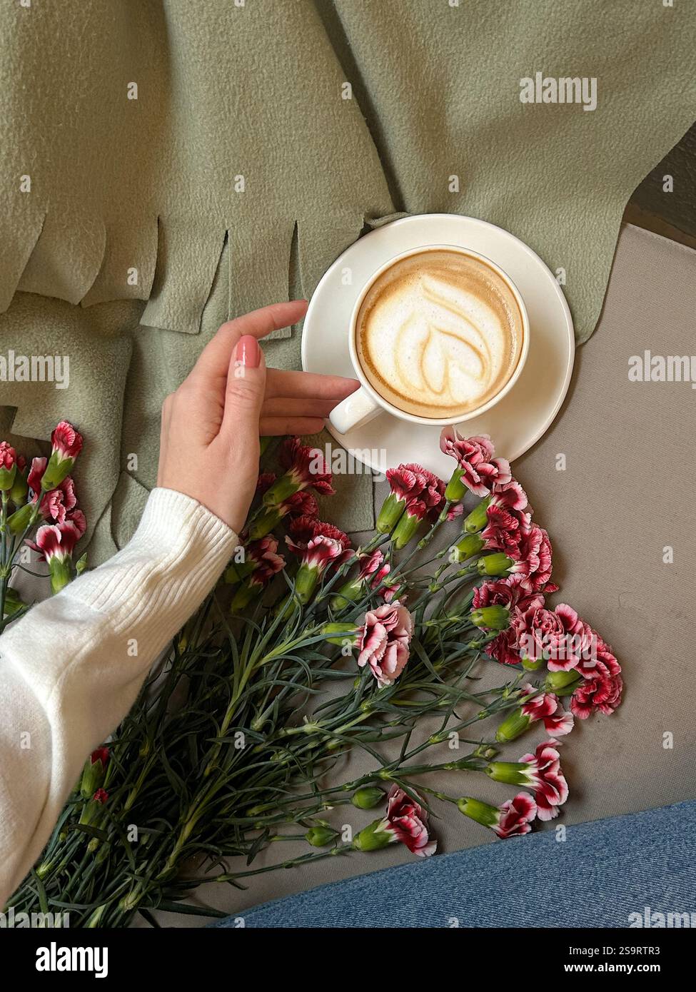 Questa elegante immagine cattura l'essenza della tranquillità e del calore. Una mano delicata raggiunge una tazza di latte bianca adornata da una schiuma a forma di cuore Foto Stock