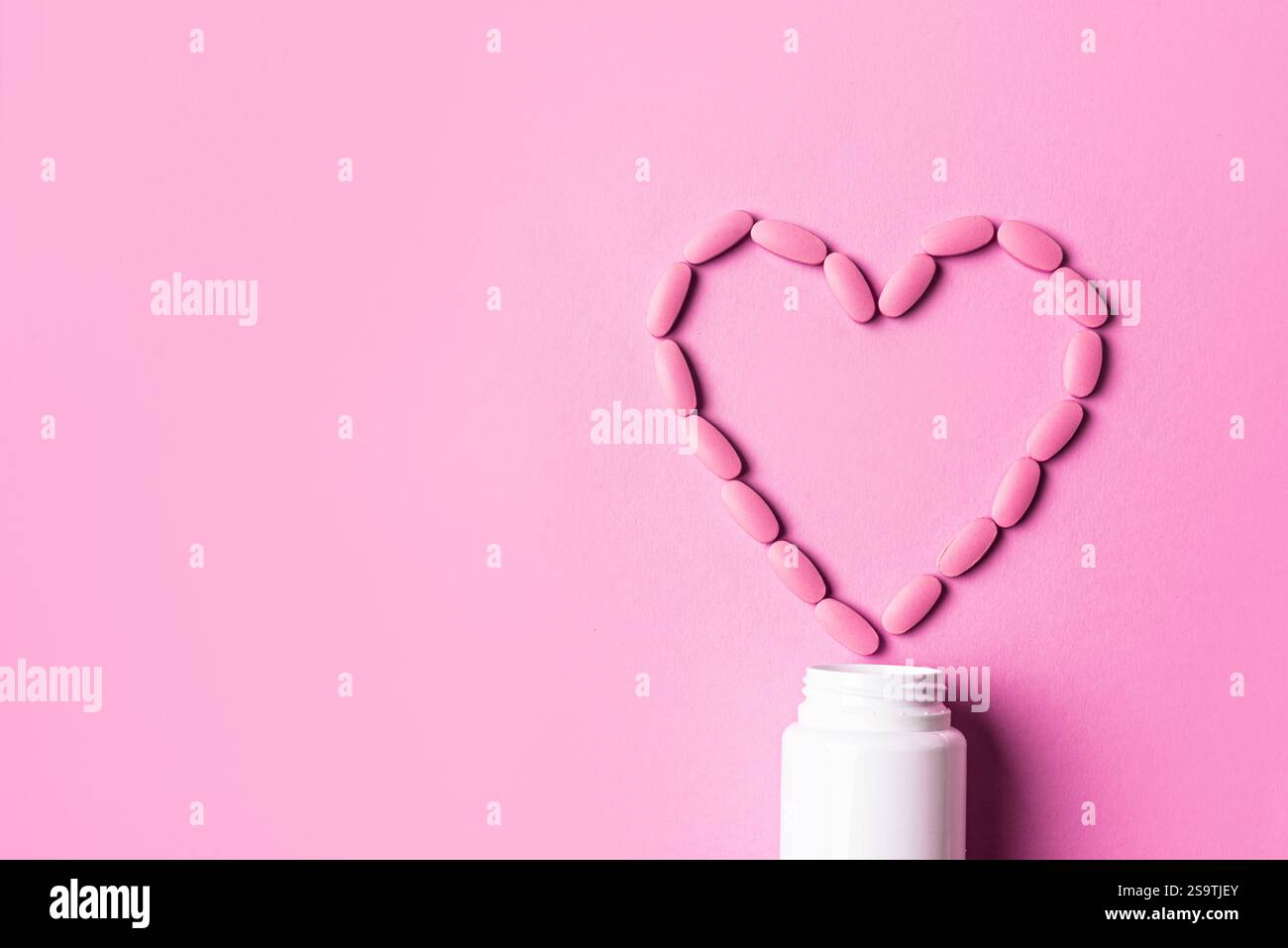 Forma del cuore fatta di pillole rosa, concetto minimo di salute cardio su sfondo rosa, vista dall'alto, spazio copia. Modello per vitamine e integratori femminili. P Foto Stock