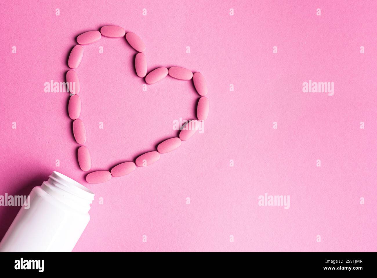 Forma del cuore fatta di pillole rosa, concetto minimo di salute cardio su sfondo rosa, vista dall'alto, spazio copia. Modello per vitamine e integratori femminili. P Foto Stock