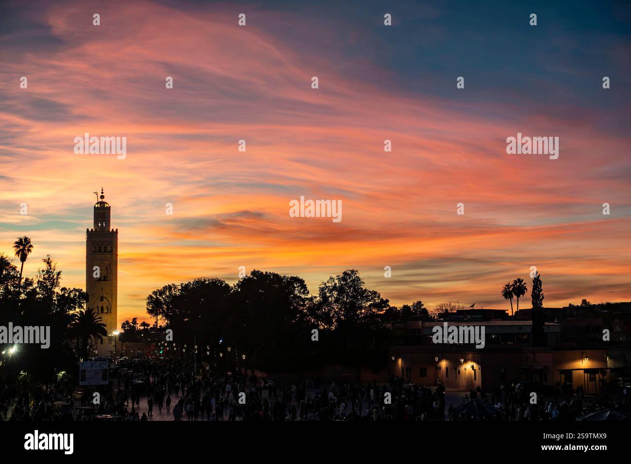 Mentre il sole tramonta, i colori vivaci riempiono il cielo di Marrakech, evidenziando la moschea di Koutoubia e la vivace attività sottostante. Foto Stock