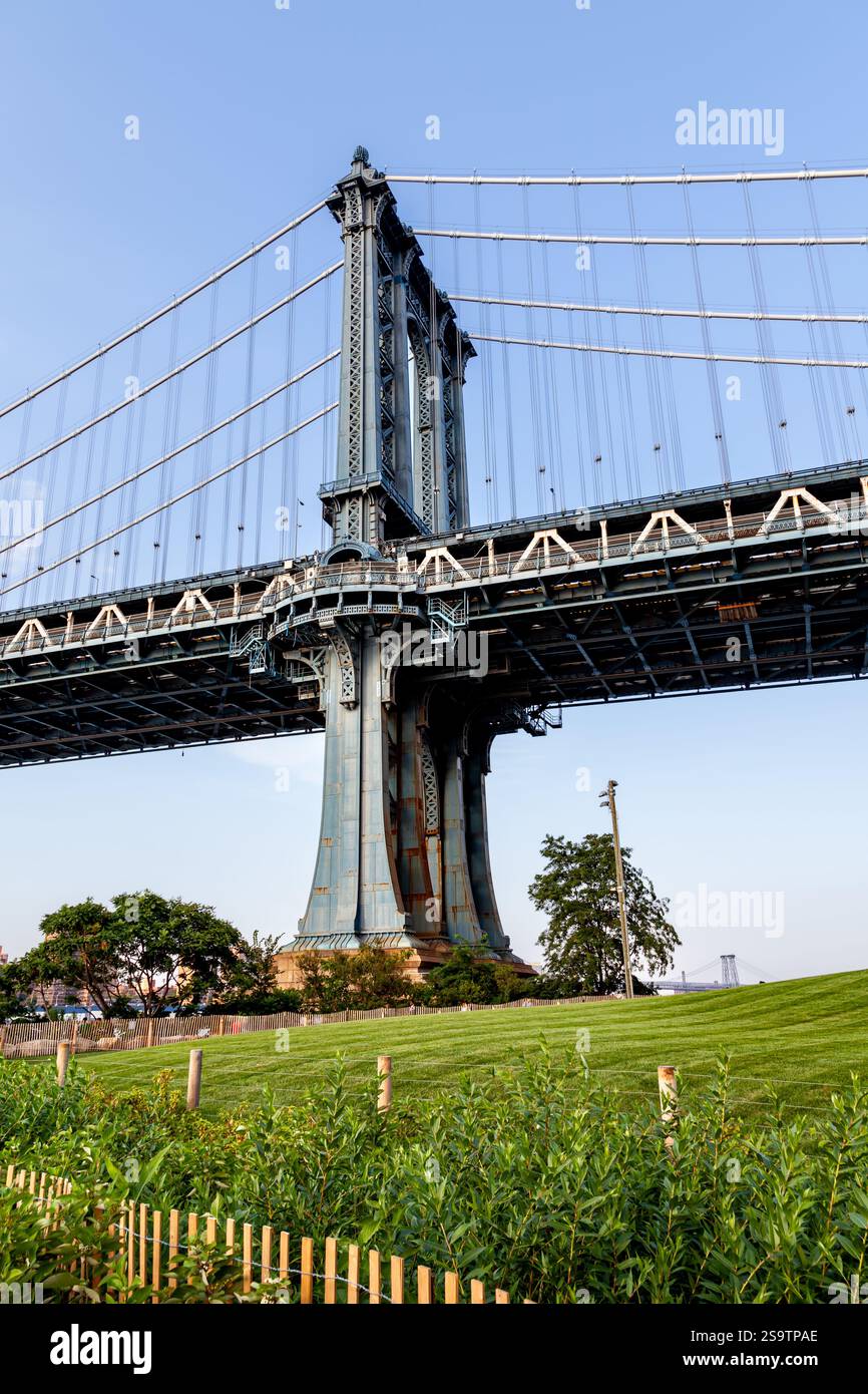 Suggestiva vista del Ponte di Manhattan che mostra la sua struttura in ferro, adagiata su uno sfondo di verde vivace in una giornata di sole a New York City Foto Stock
