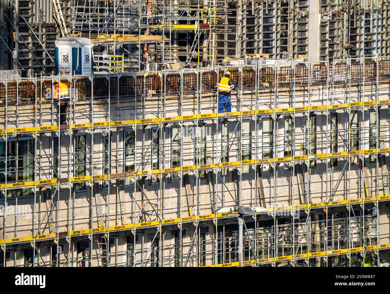 Grande cantiere, nuovo edificio circondato da ponteggi, fabbriche e uffici, lavoratori sul ponteggio durante i lavori di facciata, Foto Stock