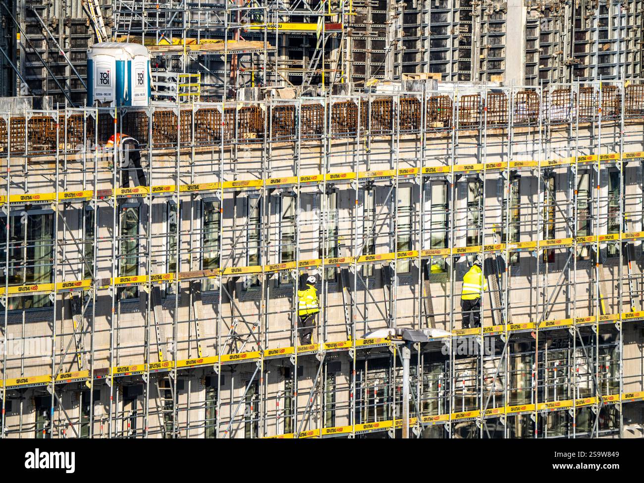 Grande cantiere, nuovo edificio circondato da ponteggi, fabbriche e uffici, lavoratori sul ponteggio durante i lavori di facciata, Foto Stock