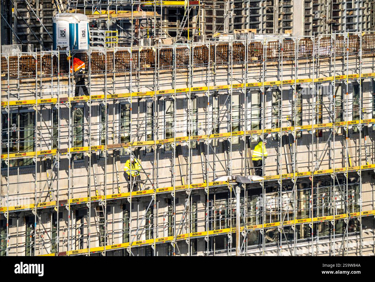 Grande cantiere, nuovo edificio circondato da ponteggi, fabbriche e uffici, lavoratori sul ponteggio durante i lavori di facciata, Foto Stock