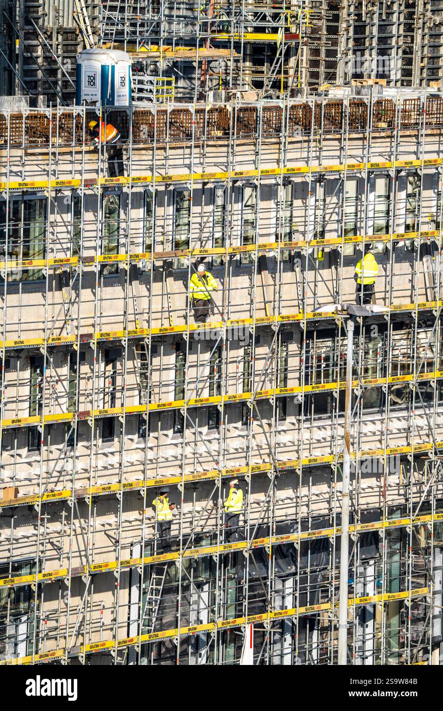 Grande cantiere, nuovo edificio circondato da ponteggi, fabbriche e uffici, lavoratori sul ponteggio durante i lavori di facciata, Foto Stock