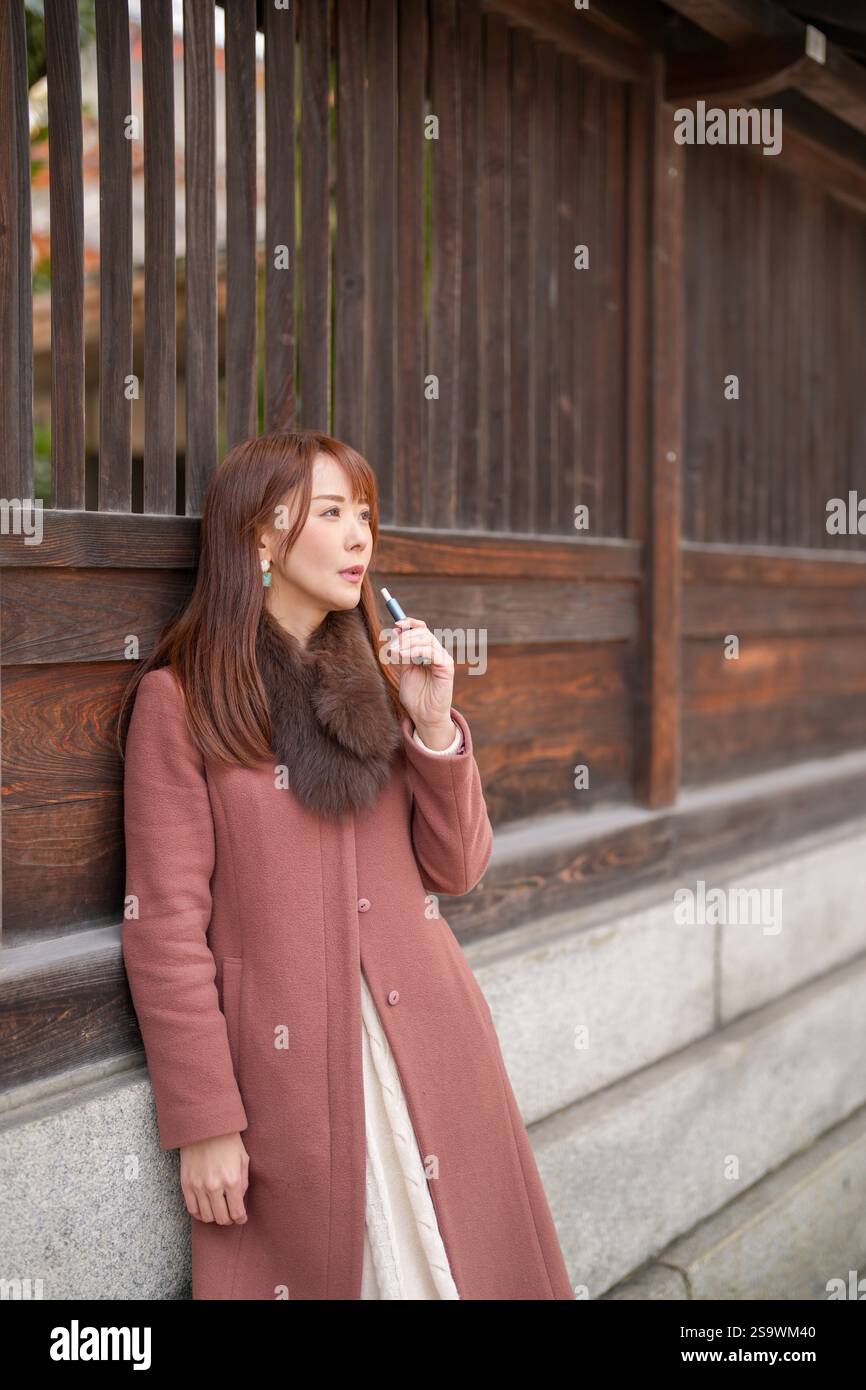 Accanto agli edifici storici in Giappone. Una donna giapponese con i capelli lunghi sui trent'anni guarda la città fumando sigarette elettroniche. Foto Stock