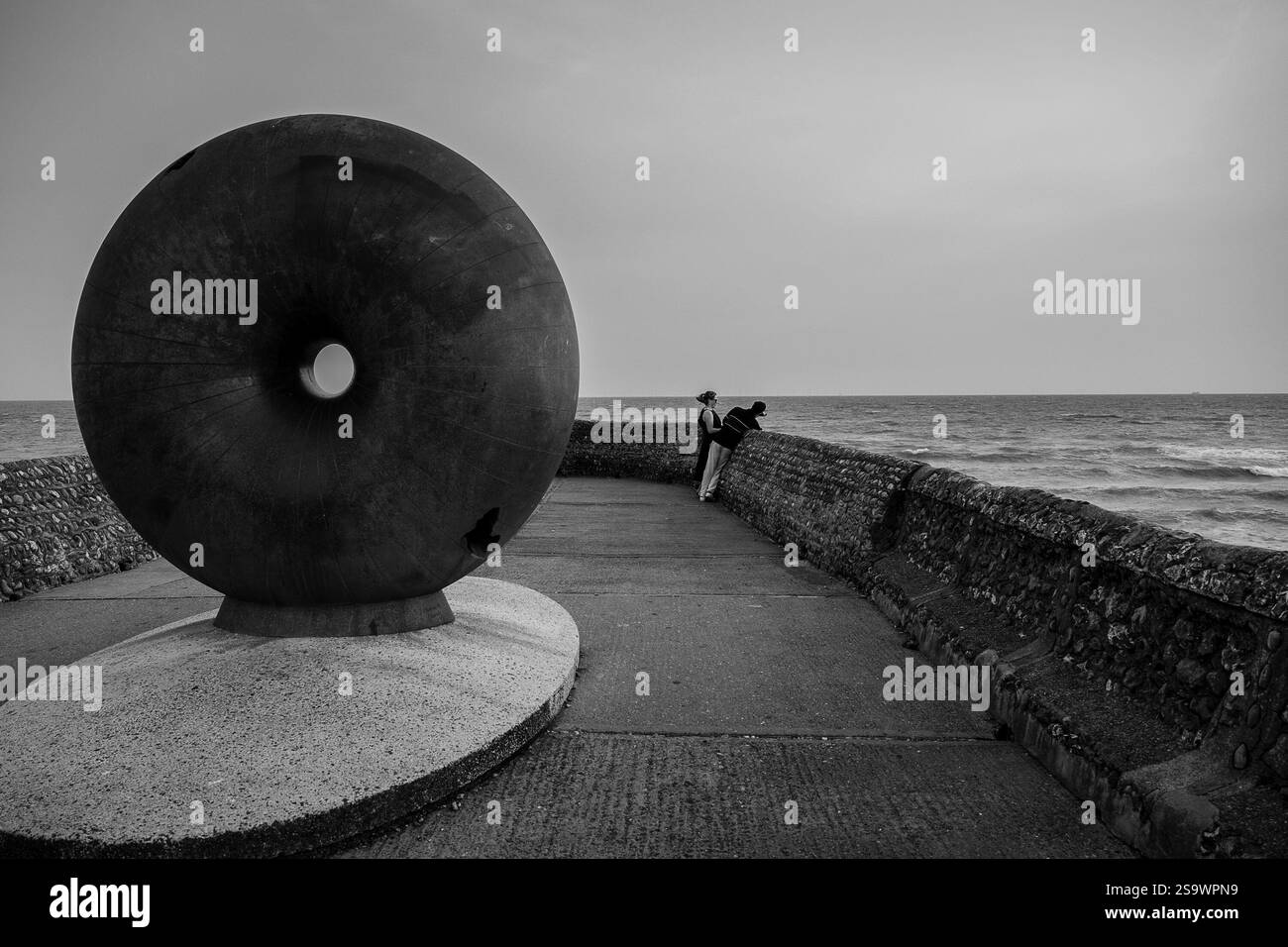 Una coppia sulla struttura Groyne sul lungomare di Brighton, vicino al Palace Pier, 'a galla' è un enorme globo a forma di ciambella circolare. Hamish Black Foto Stock