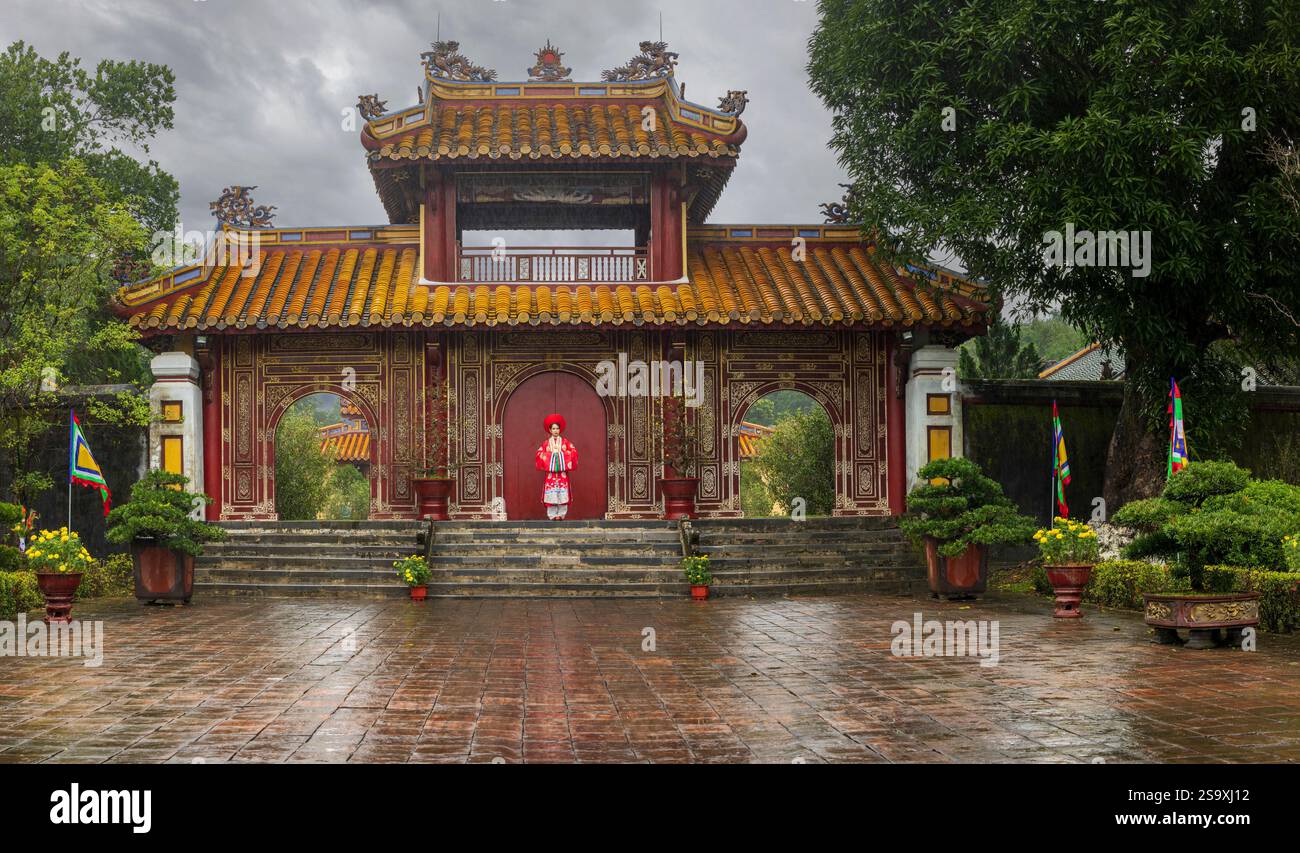 Vietnam, Hue. Giovane donna vietnamita che posa nel suo vestito per la celebrazione del nuovo anno chiamato Ao dai di fronte all'ingresso del vecchio tempio tradizionale. (SIG.) Foto Stock