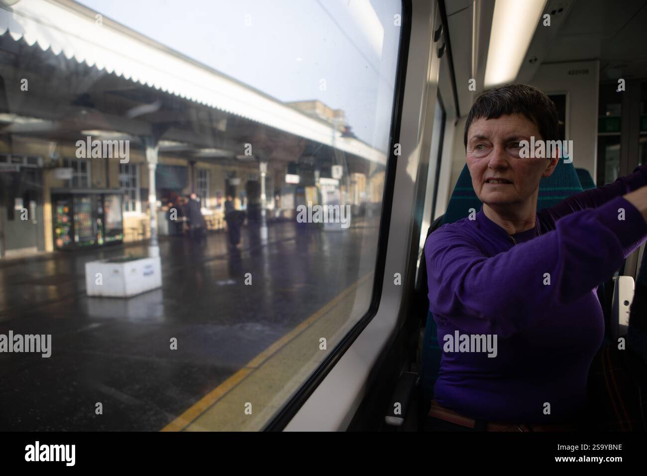 Donna in cima viola che si mette a proprio agio su un treno. Stazione ferroviaria di Ely Foto Stock